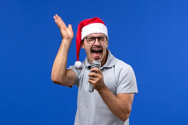 Vista frontal macho joven sosteniendo el micrófono en la pared azul cantante masculino de música de año nuevo