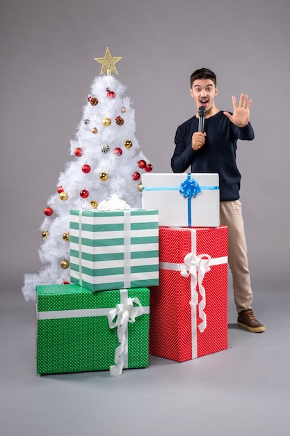 Vista frontal macho joven sosteniendo el micrófono con regalos en el gris