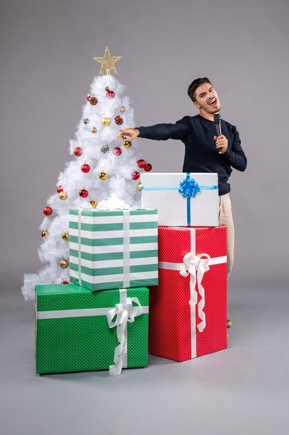 Vista frontal macho joven sosteniendo el micrófono con regalos en el gris