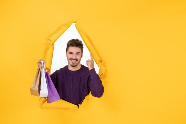 Vista frontal macho joven sosteniendo pequeños paquetes después de comprar sobre fondo amarillo regalo de vacaciones de colores de Navidad de año nuevo presente