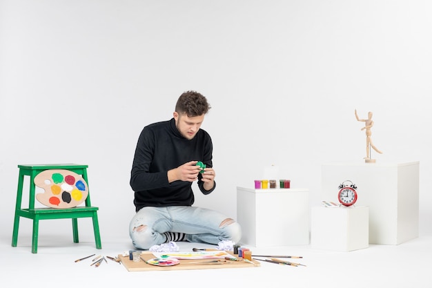 Vista frontal macho joven sosteniendo la pintura dentro de la pequeña lata en la pared blanca foto arte cuadro pintura dibujar pinturas de artistas de color