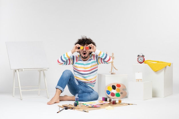 Foto gratuita vista frontal del macho joven sosteniendo pinturas para dibujar dentro de latas pequeñas en la pared blanca