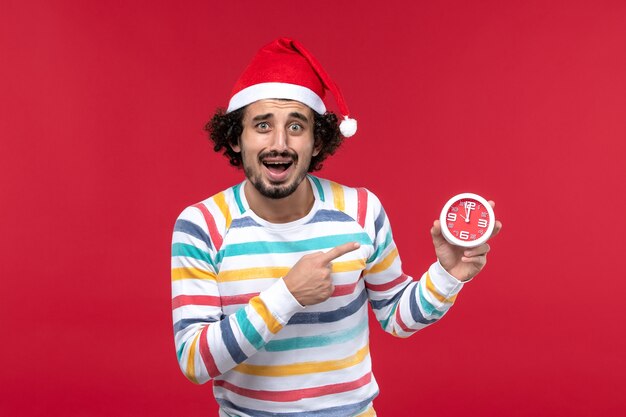 Vista frontal macho joven sosteniendo relojes redondos en la pared roja tiempo año nuevo vacaciones rojas