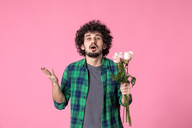 Vista frontal macho joven sosteniendo rosas rosadas en color rosa