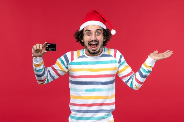 Vista frontal macho joven sosteniendo una tarjeta bancaria en la pared de color rojo claro dinero rojo emoción masculina vacaciones
