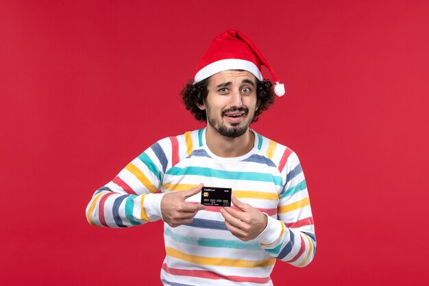 Vista frontal macho joven sosteniendo una tarjeta bancaria en la pared de color rojo claro emoción de fiesta roja masculina