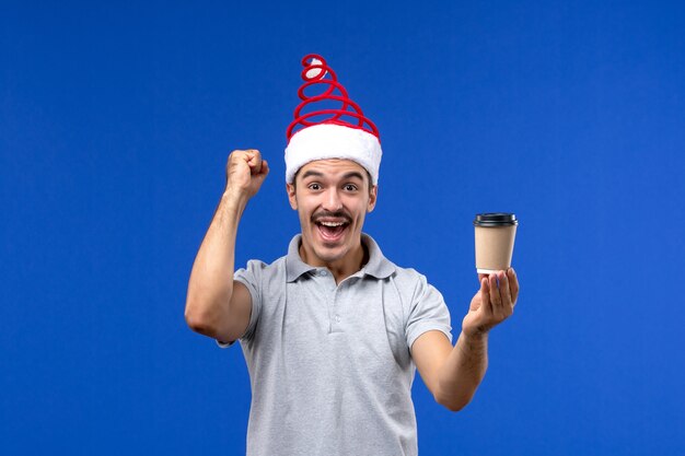 Vista frontal macho joven sosteniendo la taza de café en la pared azul emoción de vacaciones masculinas de año nuevo