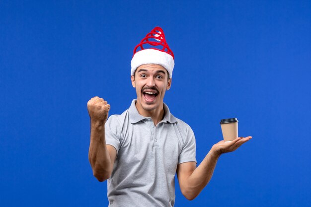 Vista frontal macho joven sosteniendo una taza de café de plástico en la pared azul emoción masculina año nuevo