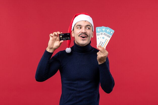 Vista frontal macho joven con tarjeta bancaria de billetes sobre fondo rojo.