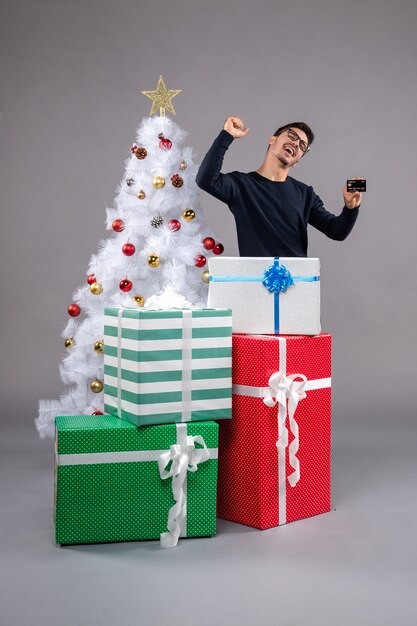 Vista frontal macho joven con tarjeta bancaria en piso ligero año nuevo regalo de navidad