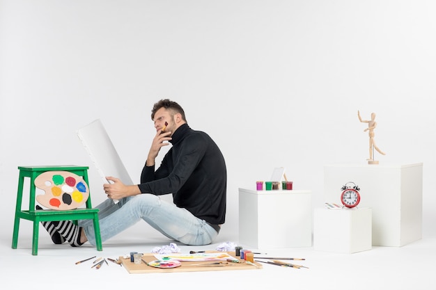 Vista frontal macho joven tratando de dibujar pintura con borla pensando en la pared blanca imagen en color pintura arte pintura dibujo artista