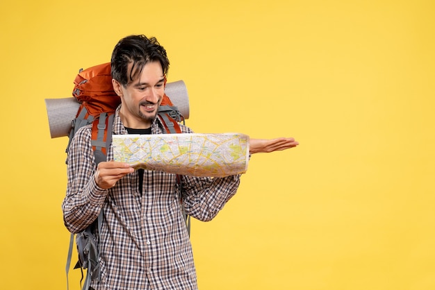 Foto gratuita vista frontal macho joven yendo de excursión con mochila observando mapa sobre fondo amarillo viaje de empresa forestal naturaleza color aire