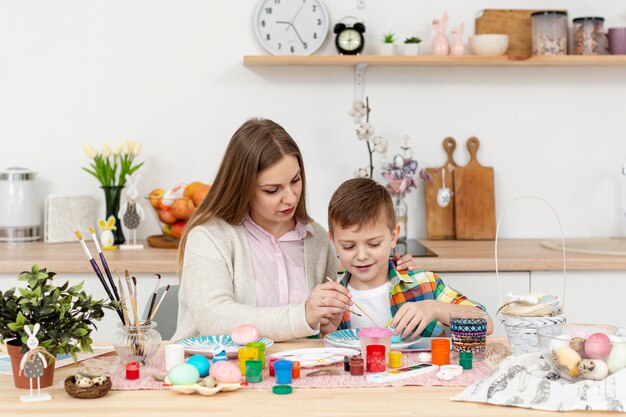 Vista frontal madre e hijo en casa pintando huevos