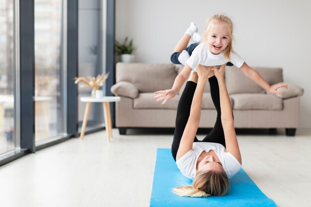 Vista frontal de la madre haciendo ejercicio con niño sonriente en casa