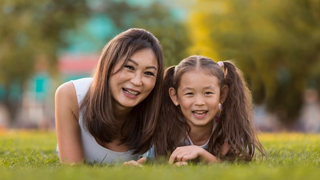 Vista frontal de la madre y la hija asiáticas permanecer juntos en el césped