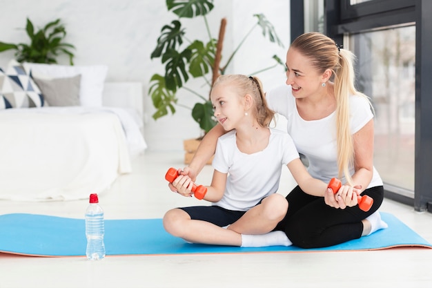 Vista frontal de la madre y la hija haciendo ejercicio con pesas en casa