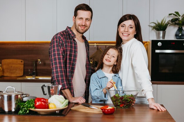 Vista frontal de la madre y el padre con la hija posando en la cocina