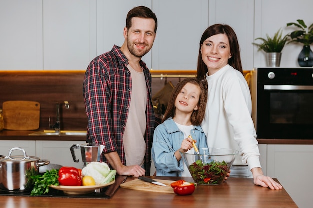 Vista frontal de la madre y el padre con la hija posando en la cocina