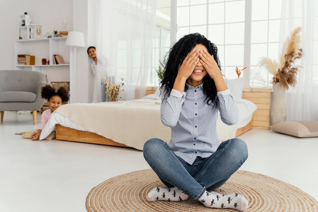 Vista frontal de la madre sonriente jugando al escondite con sus hijos en casa