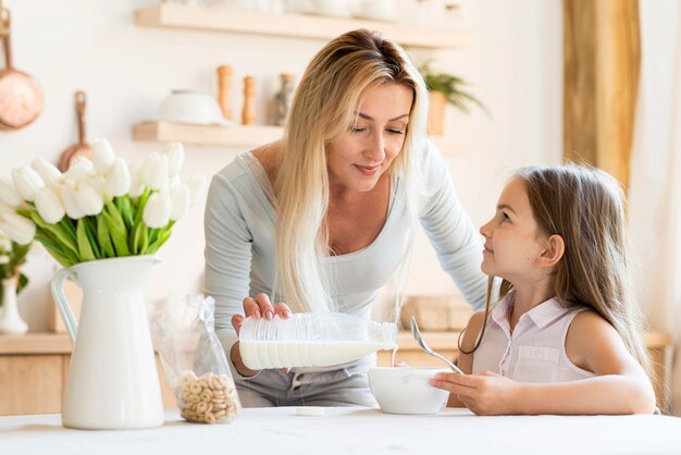 Vista frontal de la madre vertiendo leche sobre los cereales de su hija
