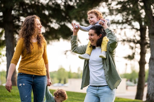 Vista frontal de madres lgbt felices afuera en el parque con sus hijos