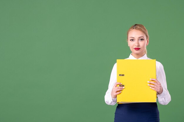Vista frontal maestra sosteniendo archivos amarillos sobre fondo verde estudio uniforme libro escuela mujer universidad lección trabajo estudiante