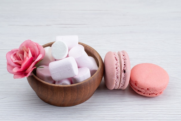 Una vista frontal de malvavisco blanco con macarons franceses rosados en el escritorio blanco, color dulce de caramelo de azúcar