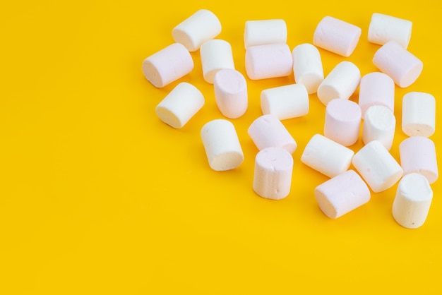 Foto gratuita una vista frontal de malvaviscos blancos deliciosos golosinas en el escritorio amarillo, color caramelo dulce de azúcar