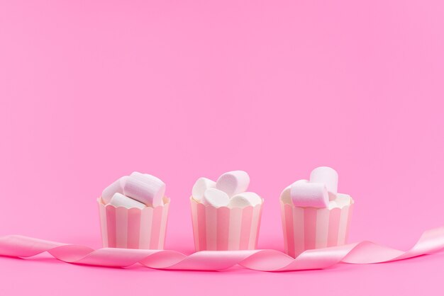 Una vista frontal de malvaviscos blancos dentro de paquetes de papel rosa aislados en rosa