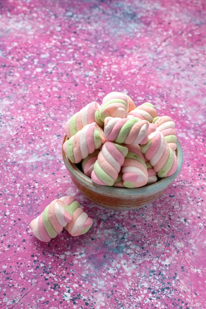 Vista frontal de malvaviscos de colores dulces poco formados dentro de una olla redonda en el escritorio rosa.