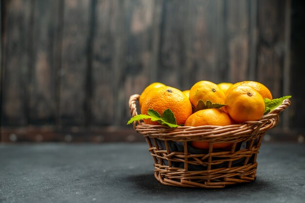 Vista frontal de mandarinas frescas en canasta de mimbre en lugar libre oscuro