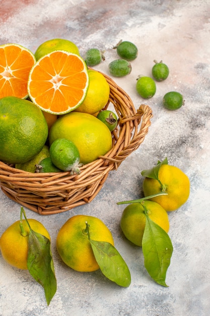 Vista frontal mandarinas frescas en cesta de mimbre rodeada de mandarinas feijoas sobre fondo desnudo