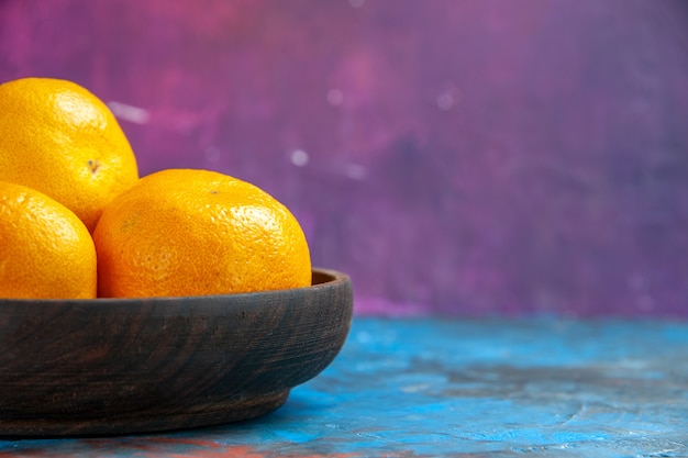 Vista frontal mandarinas frescas dentro de la placa en la mesa azul-rosa