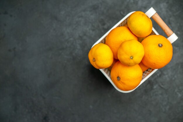 Vista frontal de mandarinas y naranjas en canasta de plástico sobre fondo oscuro espacio libre