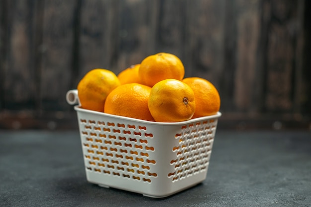 Vista frontal de mandarinas y naranjas en cesta de plastc en el espacio libre oscuro