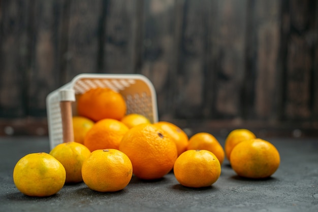 Vista frontal de mandarinas y naranjas esparcidas desde la canasta en el oscuro espacio libre