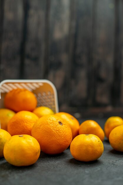 Vista frontal de mandarinas y naranjas esparcidas desde la canasta de plastc en el espacio libre oscuro