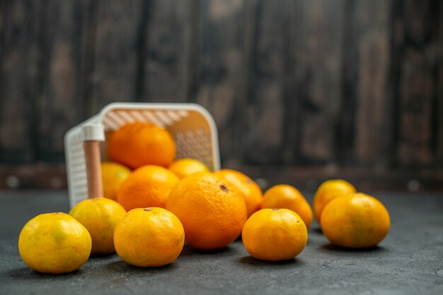 Vista frontal de mandarinas y naranjas esparcidas desde la canasta de plástico sobre fondo oscuro espacio libre