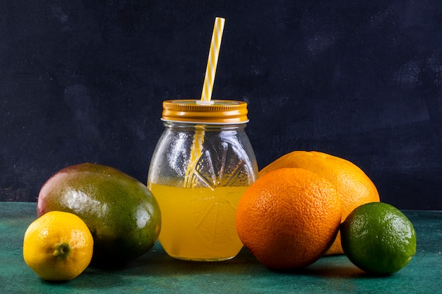 Vista frontal de mango con limón, lima, naranja y jugo en un frasco con una pajita amarilla