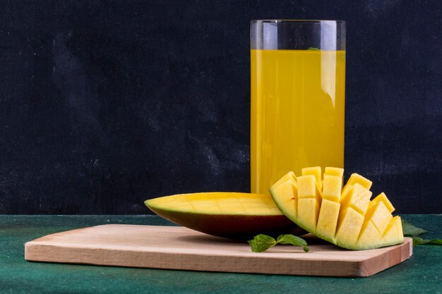 Vista frontal de mango en rodajas en la pizarra con un vaso de jugo de naranja y hojas de menta