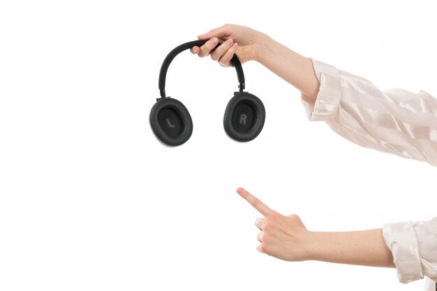 Una vista frontal de la mano femenina con auriculares negros que muestra señal de señalar en el blanco