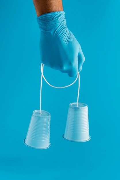 Vista frontal de la mano con guante sosteniendo vasos de plástico con cuerda