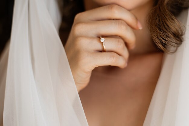 Vista frontal de la mano de la novia con un anillo de compromiso cerca del cuello y velo de novia