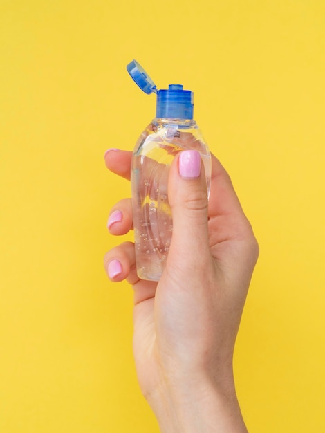 Vista frontal de la mano que sostiene la botella de plástico con desinfectante para manos