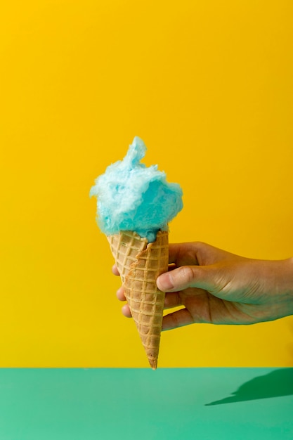 Vista frontal de la mano que sostiene el cono de helado con algodón de azúcar