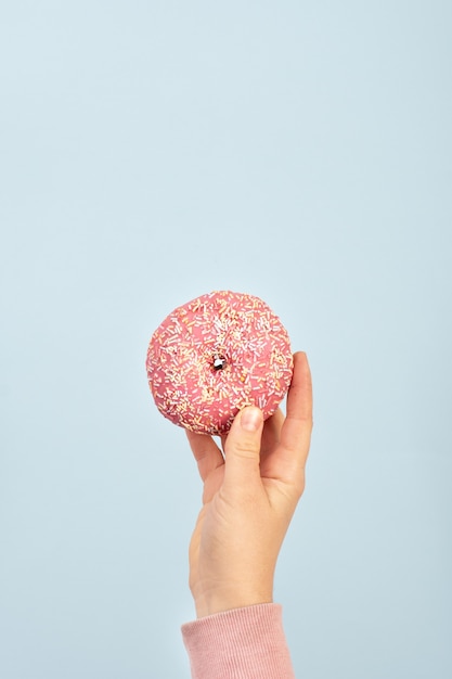 Vista frontal de la mano que sostiene donut glaseado con chispas