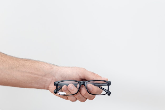 Foto gratuita vista frontal de la mano que sostiene un par de gafas con espacio de copia