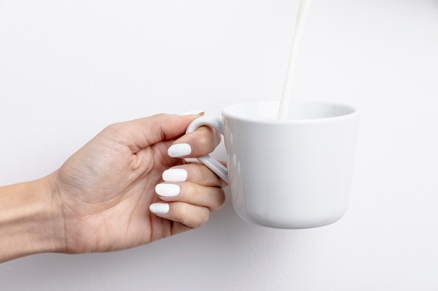Vista frontal de la mano que sostiene la taza con leche