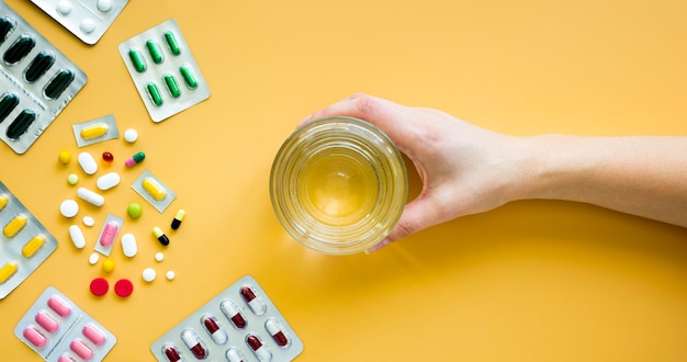 Foto gratuita vista frontal de la mano que sostiene un vaso de agua con pastillas y láminas