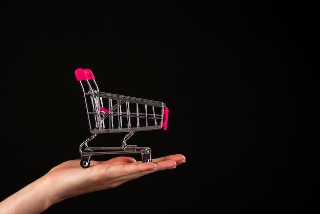 Foto gratuita vista frontal de una mano sosteniendo un mini carrito de compras sobre un fondo negro